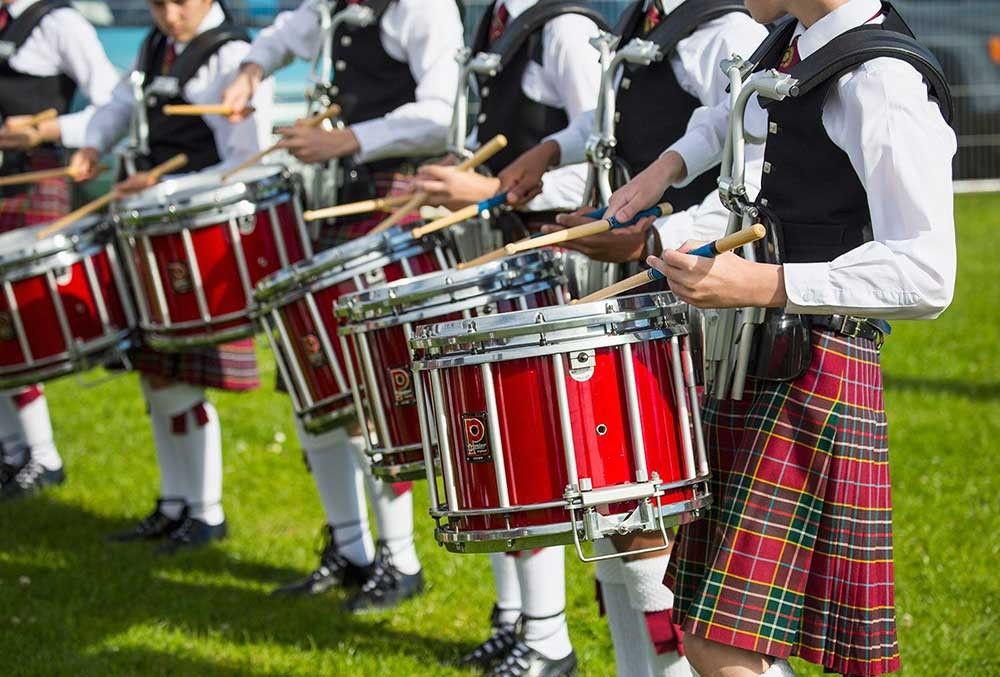 A line of Scottish drummers playing in kilts and waist coats outside.