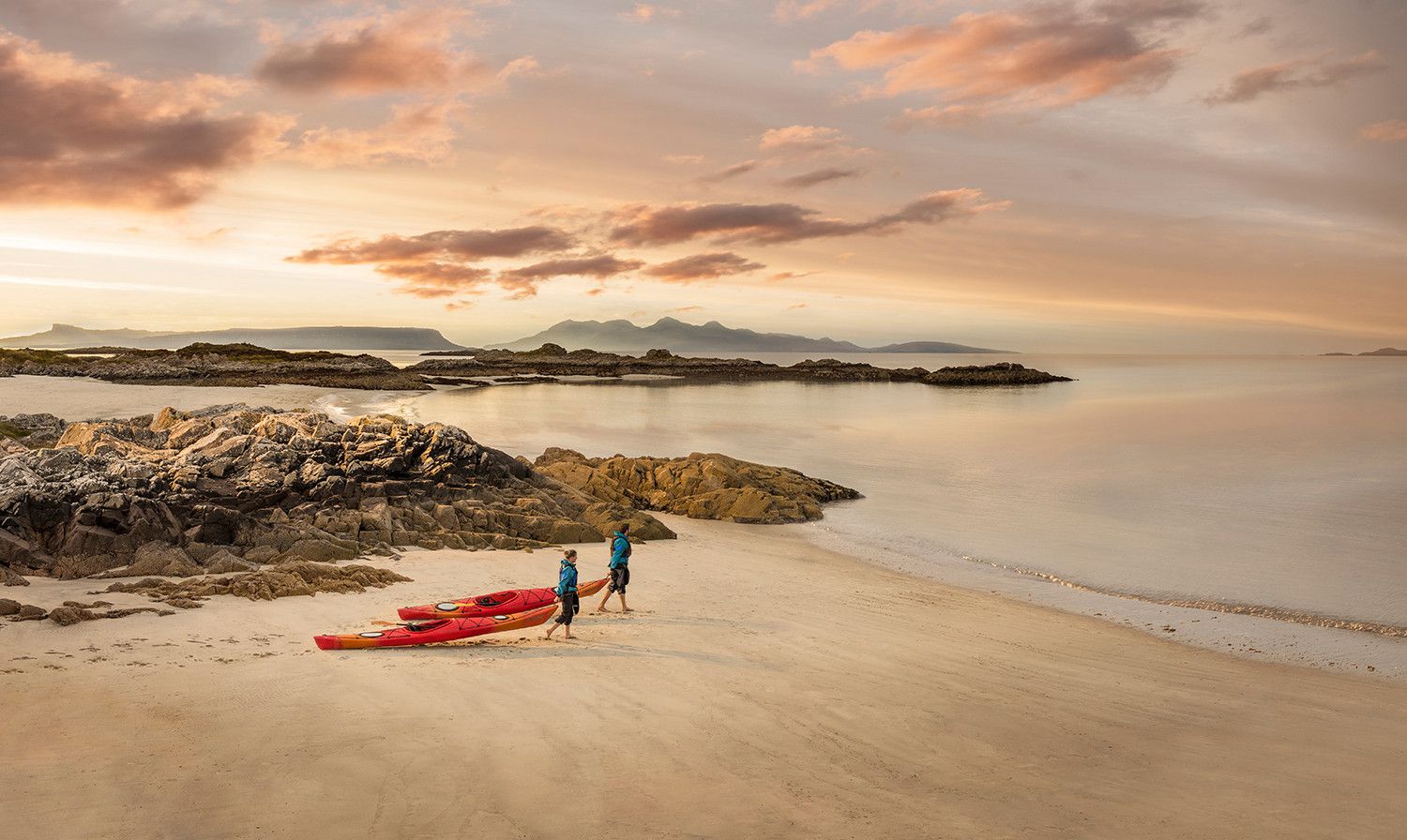 Kayakers head to the sea with their kayaks on Cambusdarach beach,