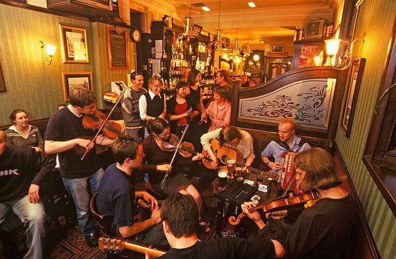 Musicians playing instruments such as guitars, violins and an accordion in a traditional Scottish pub.